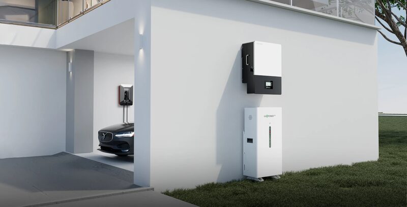 A LuxpowerTek hybrid inverter and battery unit mounted on the exterior wall of a modern house, with an EV charger and car in the garage behind
