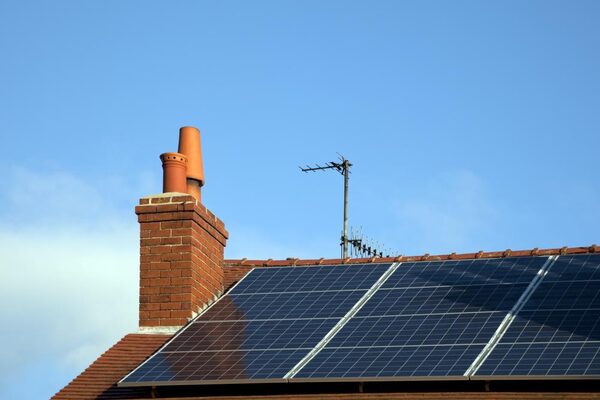 Solar panels installed on a tiled house roof beside a brick chimney and TV aerial