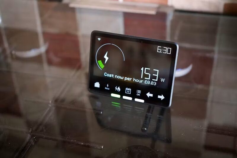 A smart meter in-home display standing on a glass table showing 153W usage and cost per hour