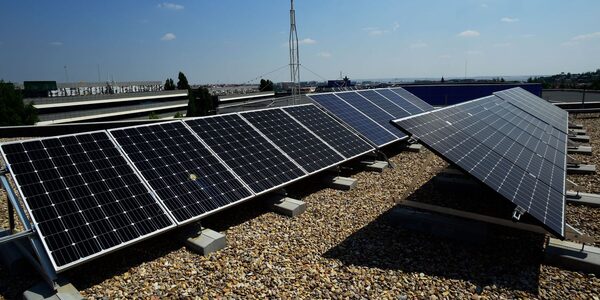 Rows of solar panels mounted on a flat gravel-covered roof under a blue sky