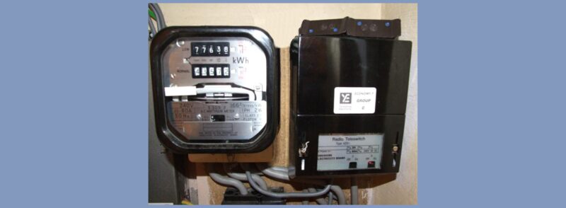 An old electricity meter mounted next to a black Radio Teleswitch box on a wall