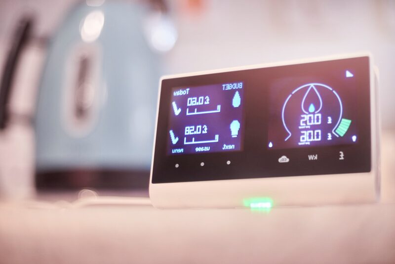 A smart meter in-home display showing energy usage and cost, with a kettle blurred in the background